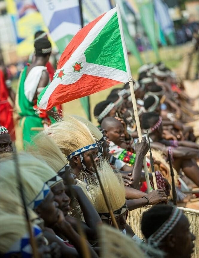 The Intore group sitting down one next to another one of them lifting a Burundian flag