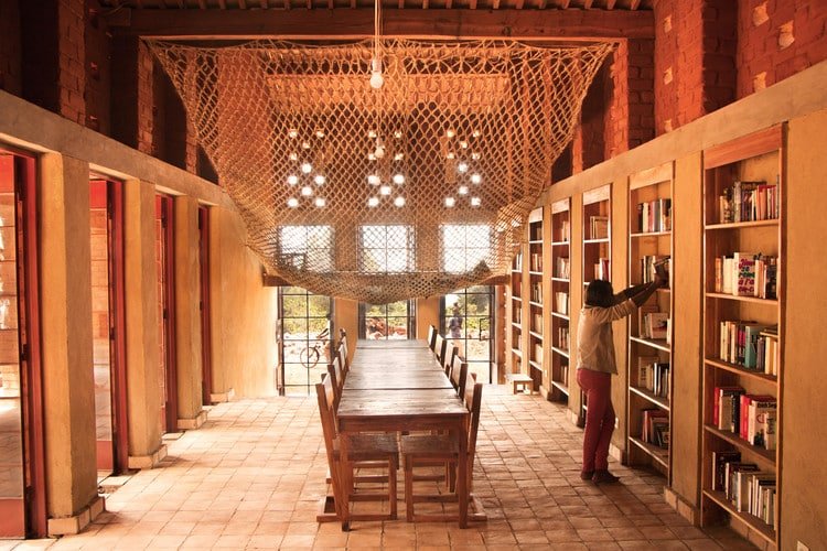 A room where there is a spot on which readers can sit and a guy arranging the books in the shelves